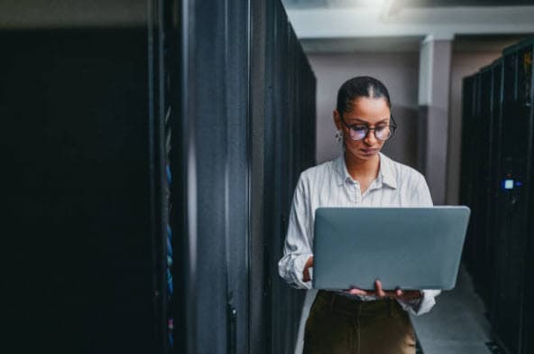 IT professional using a laptop between server racks