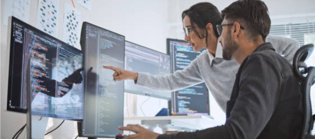 Two IT professionals reviewing code together at multiple monitors